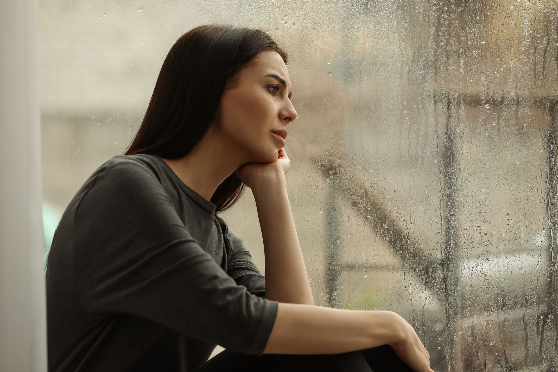 Woman sitting alone looking out a rainy window, reflecting on why its hard to leave a narcissist
