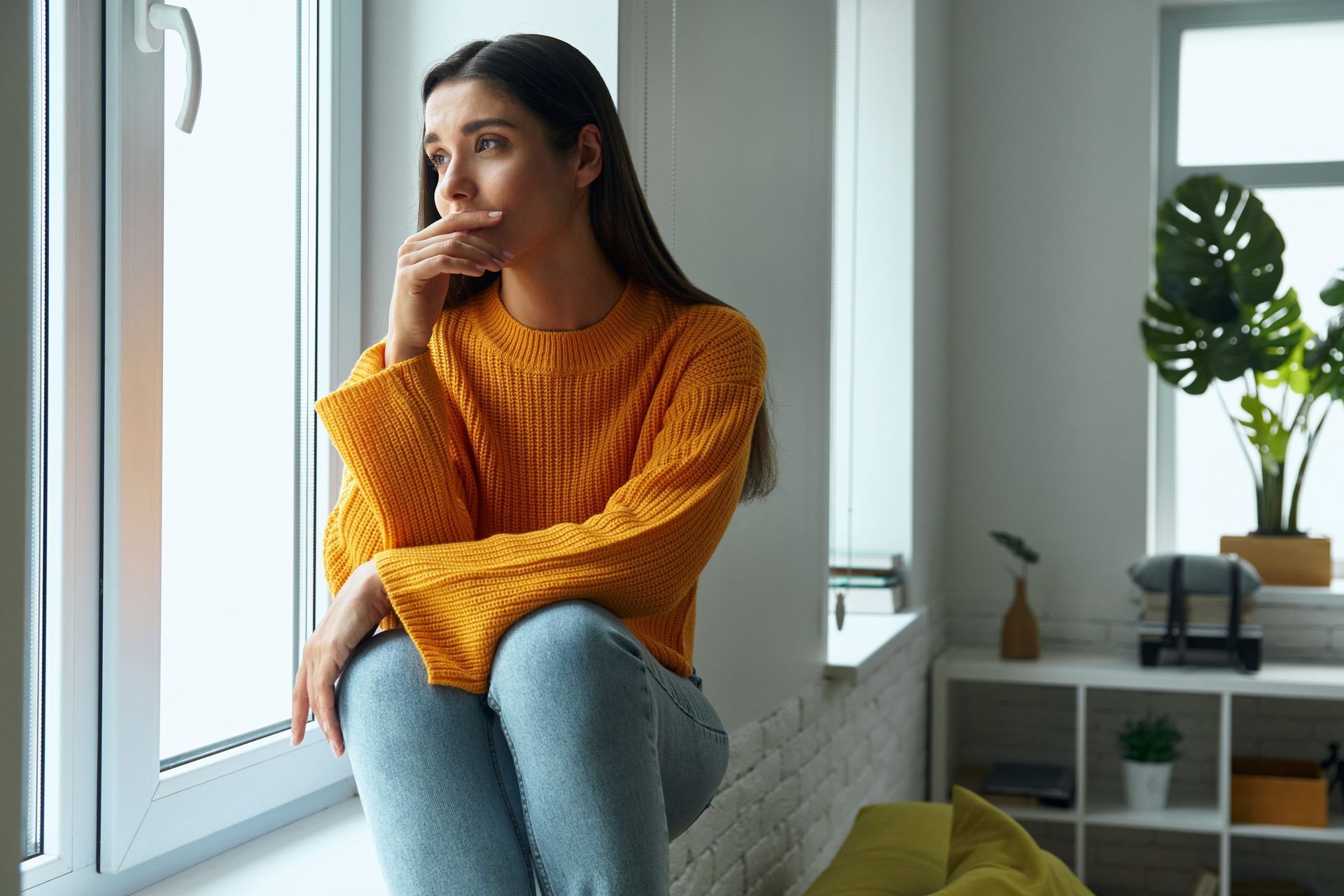 Woman sitting by a window reflecting on signs of being raised by a narcissist and adult life effects