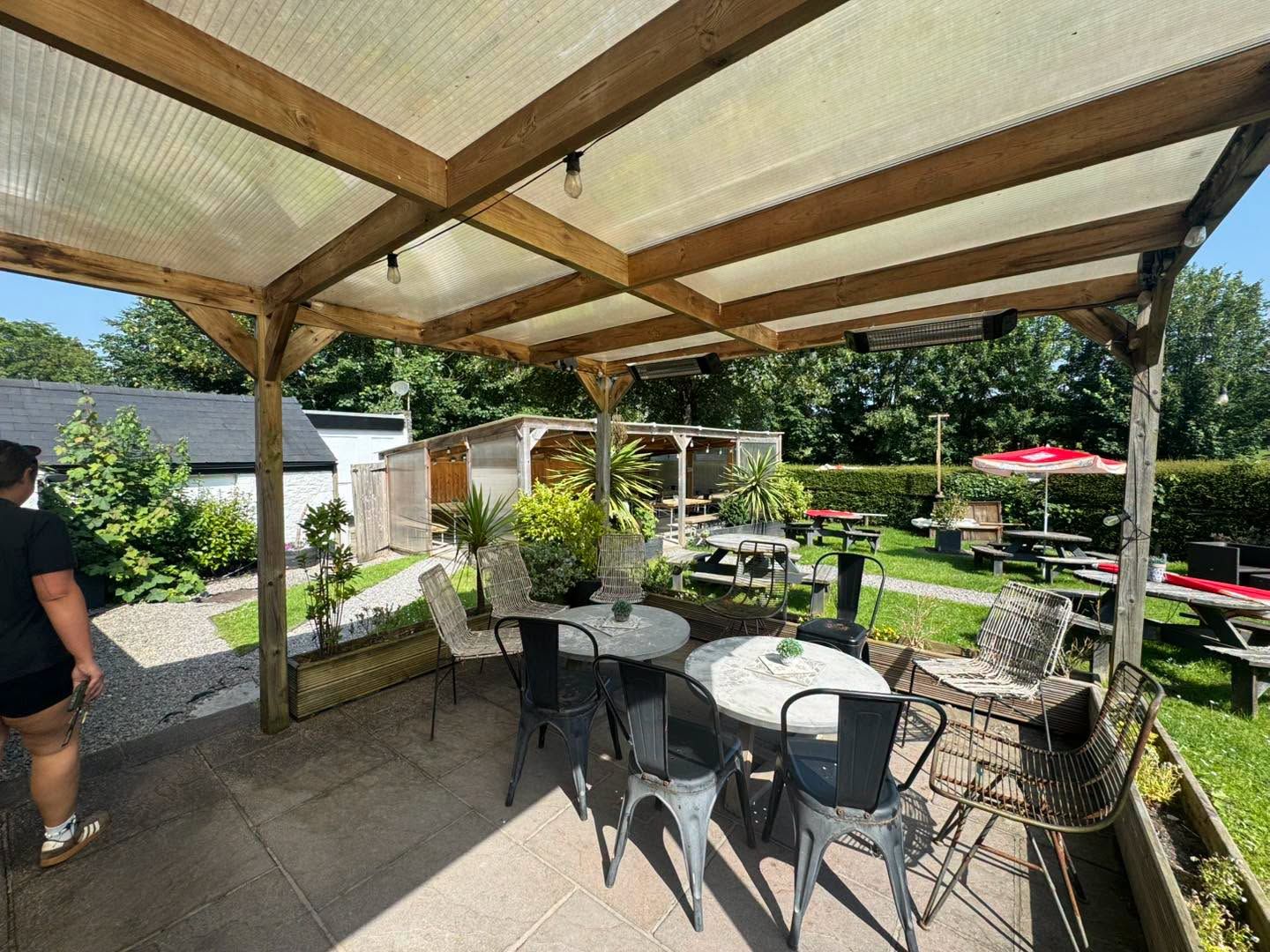 The Bush Inn, St Hilary | Covered patio with table & chairs, overlooking a sunny garden with picnic benches
& red umbrellas.