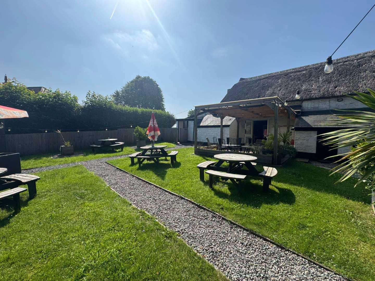 The Bush Inn, St Hilary, Cowbridge | Sunny garden with picnic tables, green lawn, gravel path, and a cottage under a blue sky