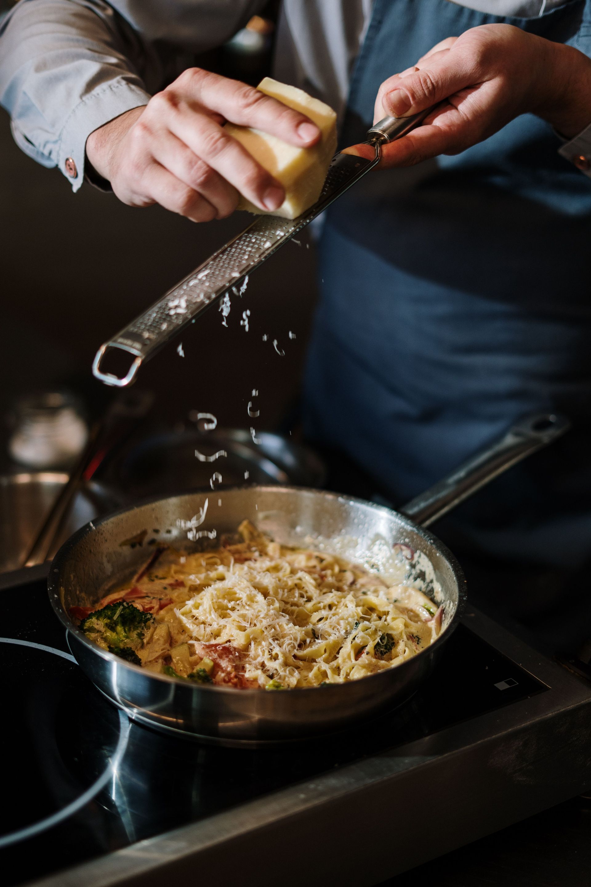 The Bush Inn, St Hilary, Cowbridge | Person grating cheese over a pan of pasta on a stovetop
