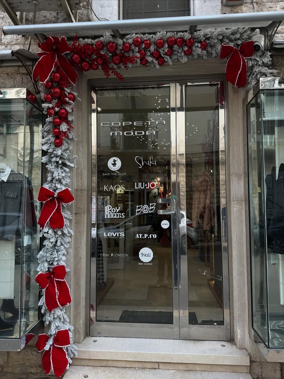 La vetrina d'ingresso del negozio è decorata con ghirlande e fiocchi natalizi rossi e argentati.