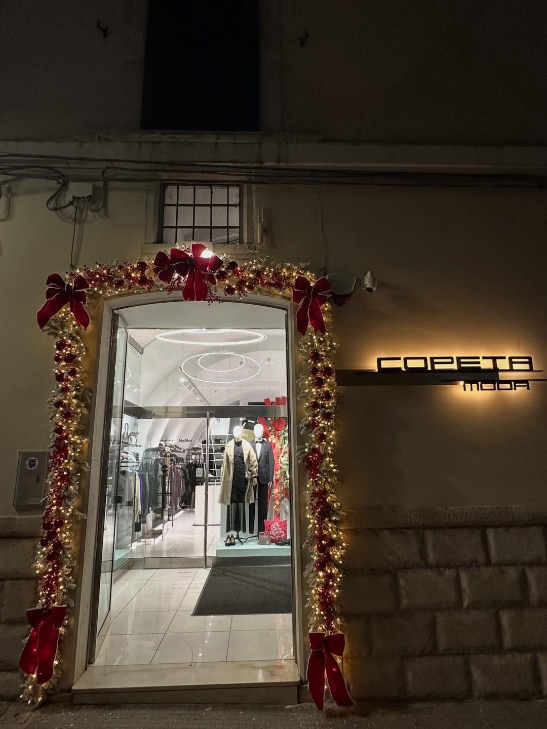 Ingresso di un negozio di abbigliamento, addobbato con ghirlande festive di notte, con interni luminosi ben visibili.