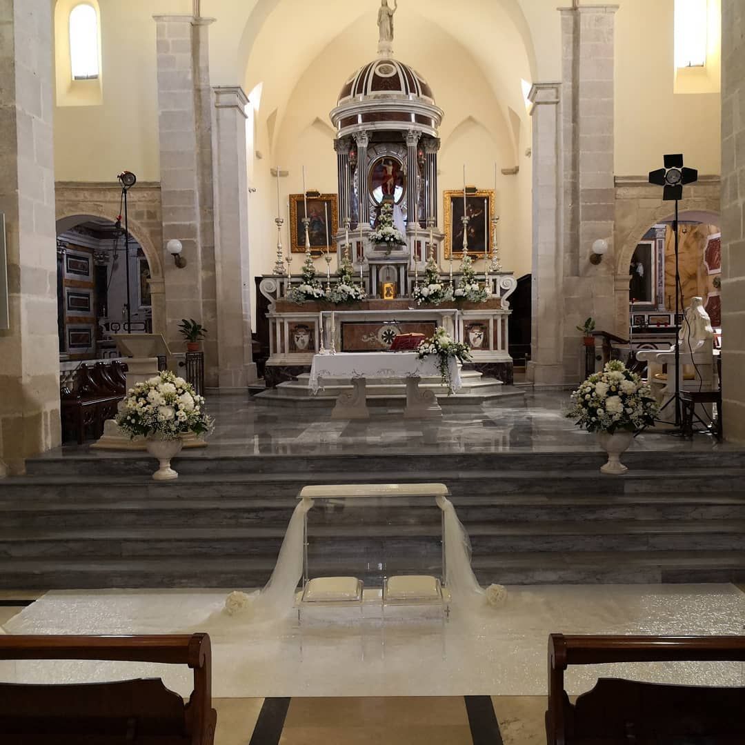 Altare della chiesa all'interno di una navata in pietra, con scalini, composizioni floreali e elaborate decorazioni religiose.