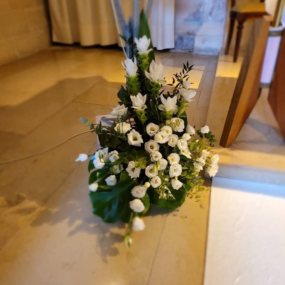 Composizione floreale bianca con verde in un vaso su un pavimento interno vicino a una porta.