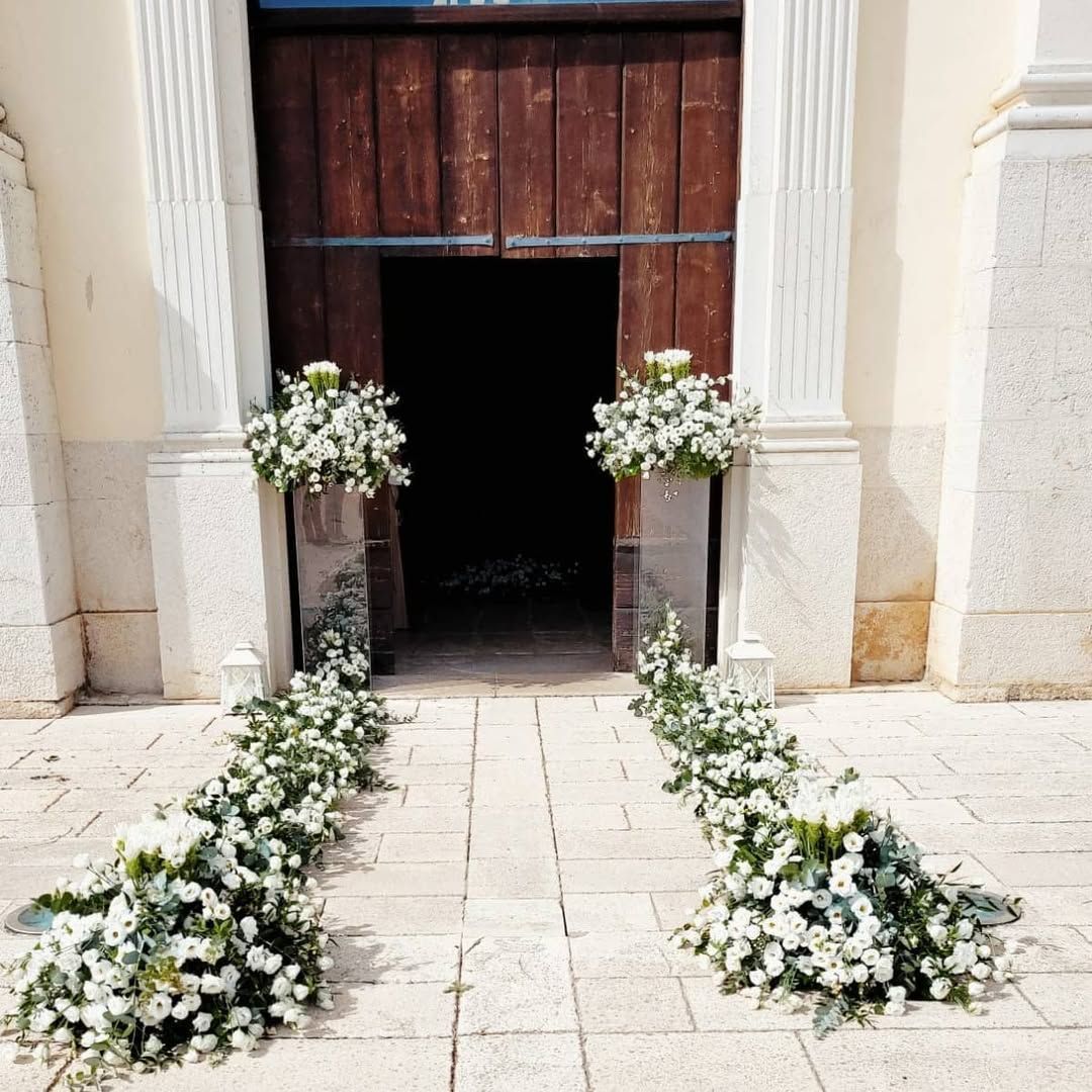 Nastra nuziale decorata con fiori bianchi che conduce a un portale in legno scuro della chiesa.