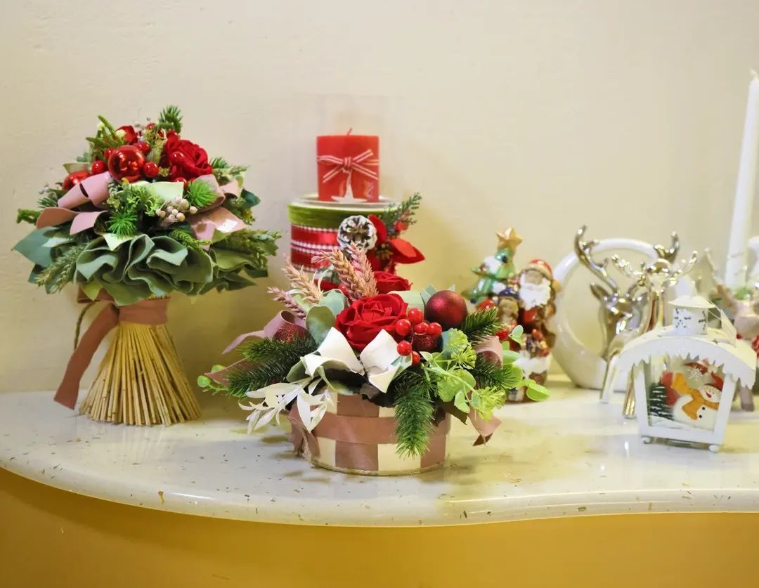 Composizione floreale natalizia e festosa per regali con bacche rosse, verde e renne decorative su un tavolo.