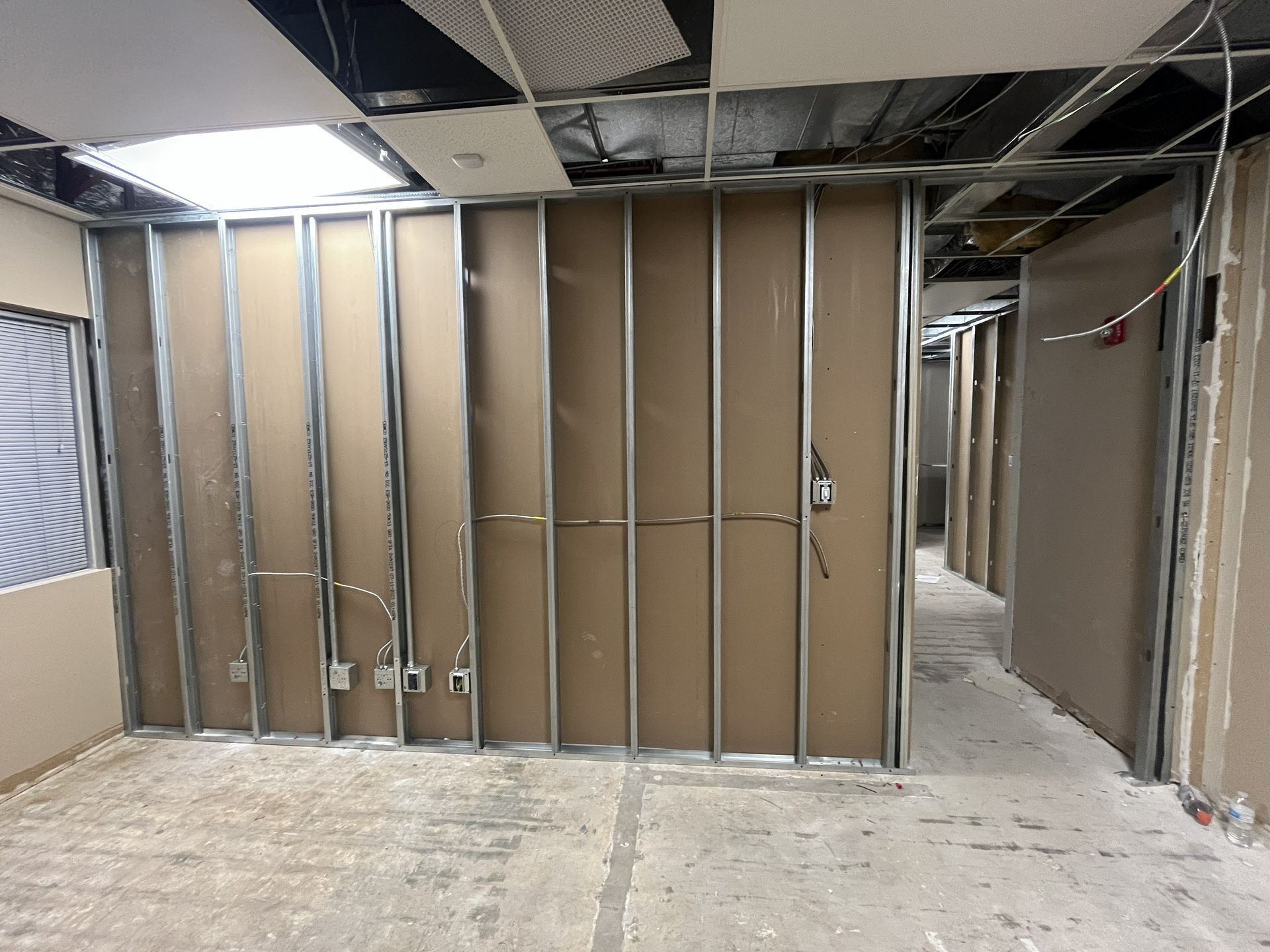 Interior office under construction; metal studs with drywall partially installed; wires exposed.