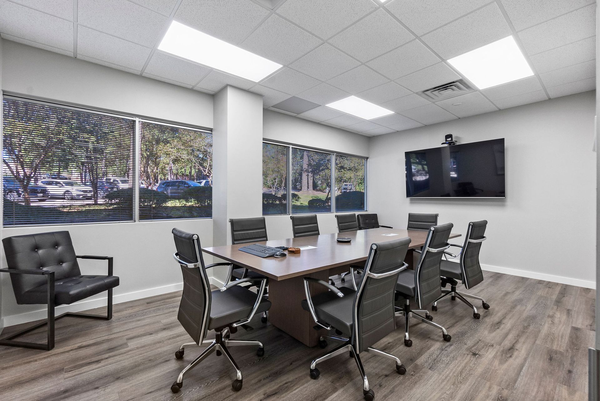 Conference room with large table, chairs, TV, windows with blinds, neutral colors.