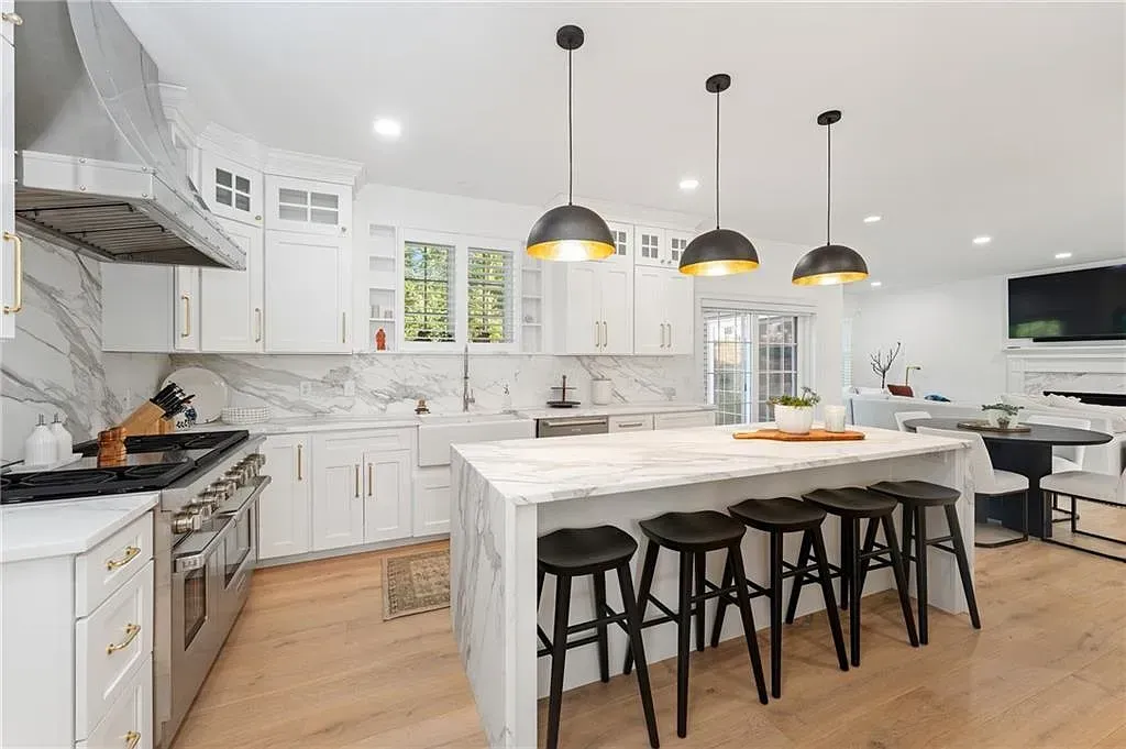 Bright modern white kitchen with island, black stools, and hanging pendant lights