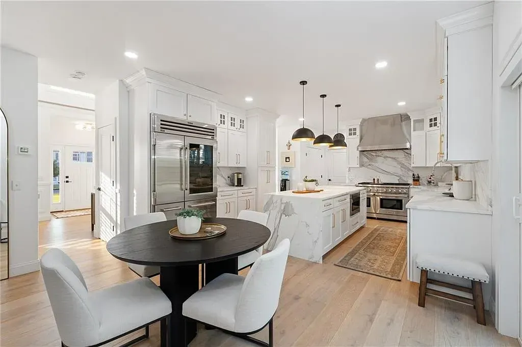 Bright white open-concept kitchen and dining area with black round table and stainless steel appliances