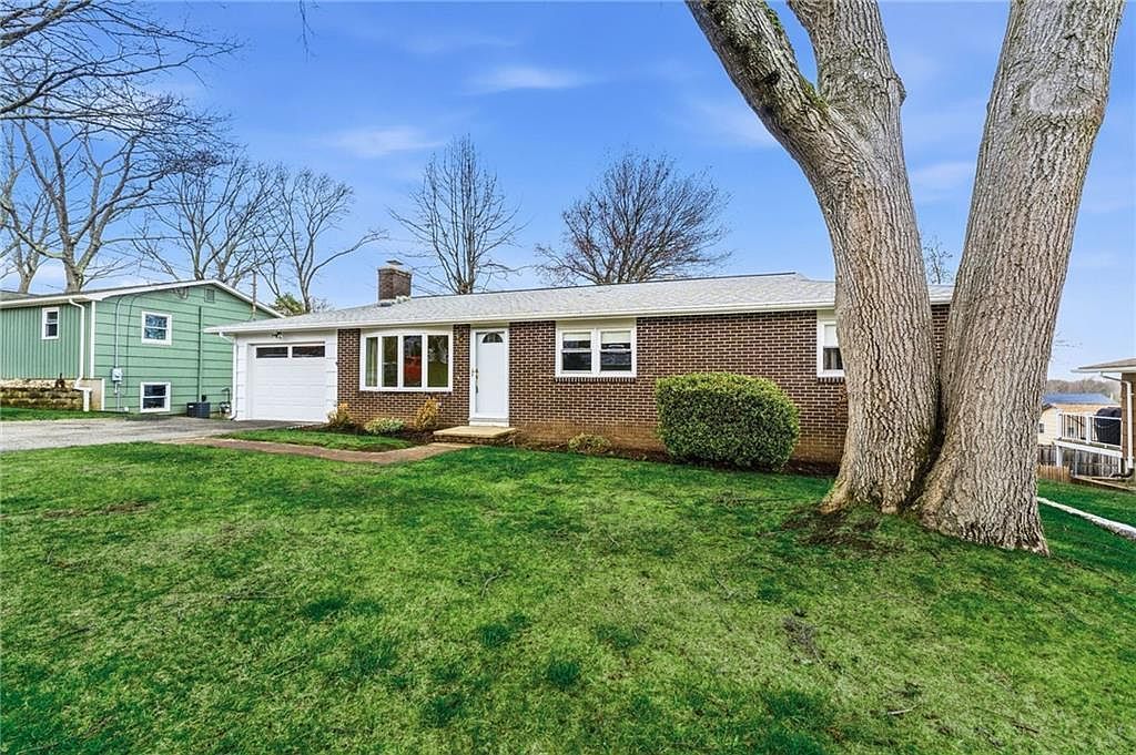 Single-story brick house with white trim, green lawn, and two large trees in the front yard
