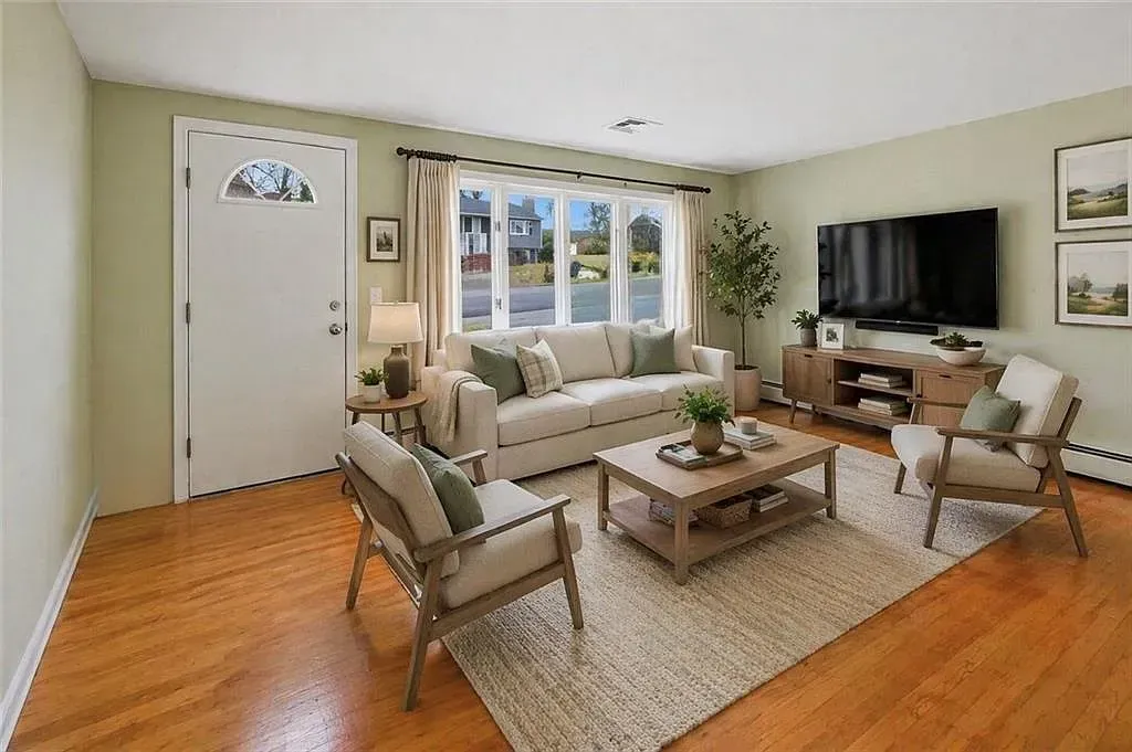 Bright living room with beige furniture, wood floors, large windows, and a TV on the wall