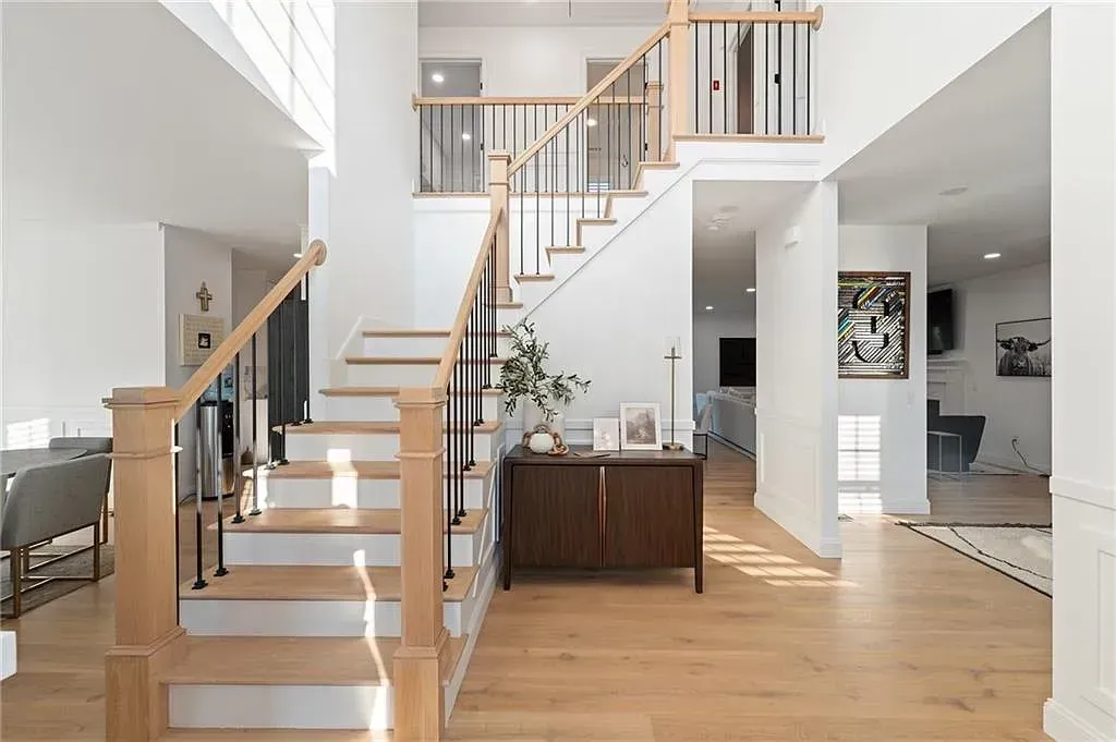 Bright modern foyer with wooden staircase, open loft railing, and sunlit hardwood floors