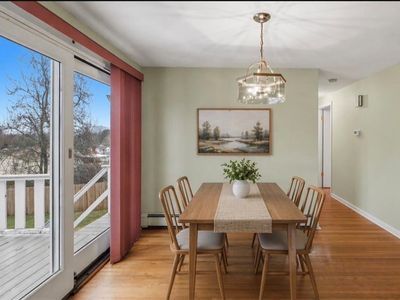 Dining room with wooden table, chairs, hanging light, and sliding glass door to a porch overlooking trees.