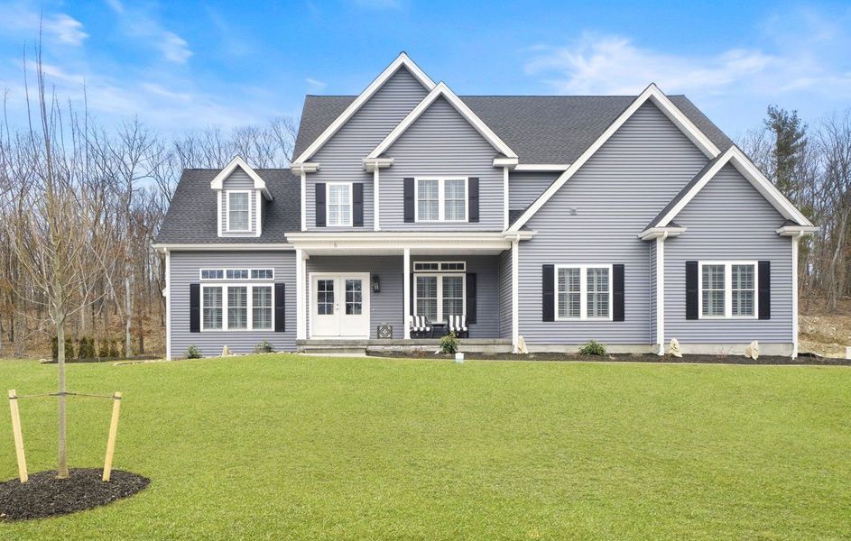 Gray two-story house with black shutters, white trim, and a porch, on a green lawn under a blue sky.