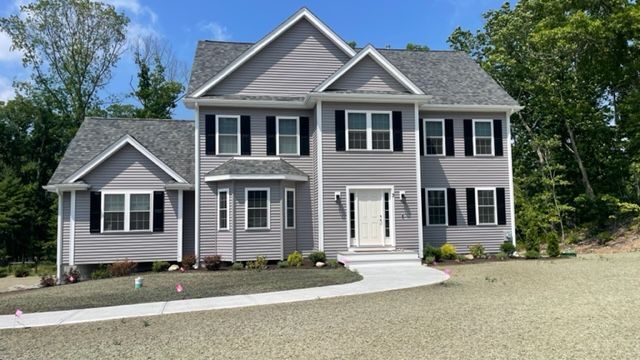 Gray two-story house with black shutters, white door, and a concrete driveway on a sunny day.