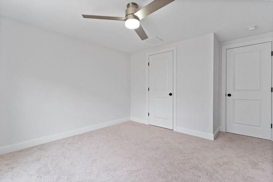 Empty bedroom with white walls, carpet, two doors, and a ceiling fan.