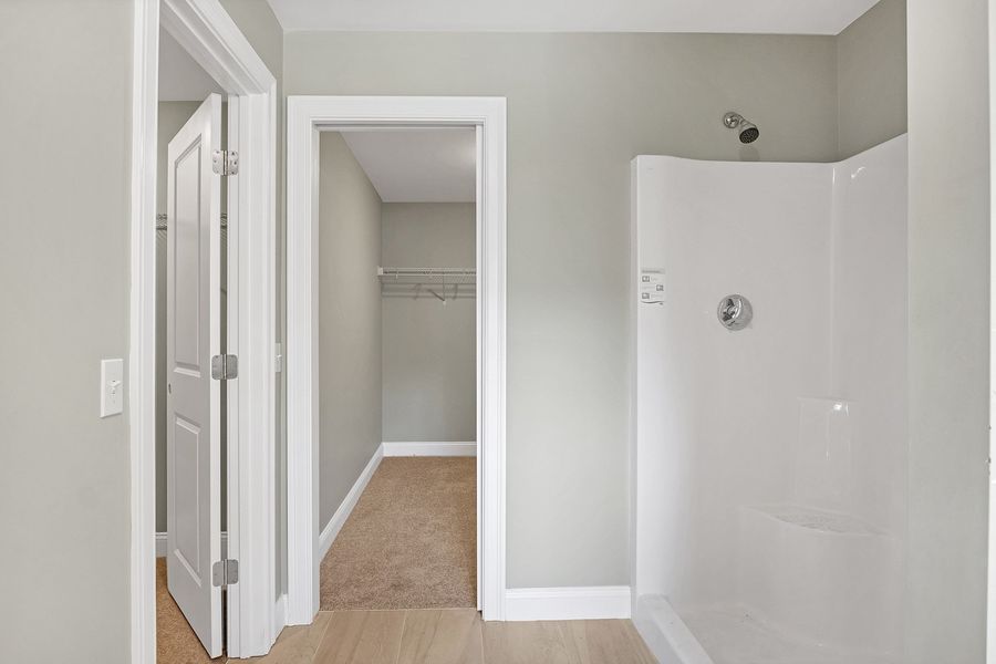 Bathroom with shower stall, open closet, and doorway on light green walls with wood-look flooring.