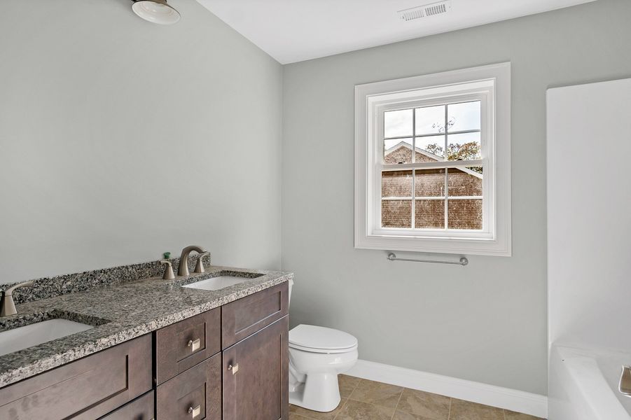 Bathroom with double vanity, toilet, and window. Gray walls, brown cabinets, and a granite countertop.