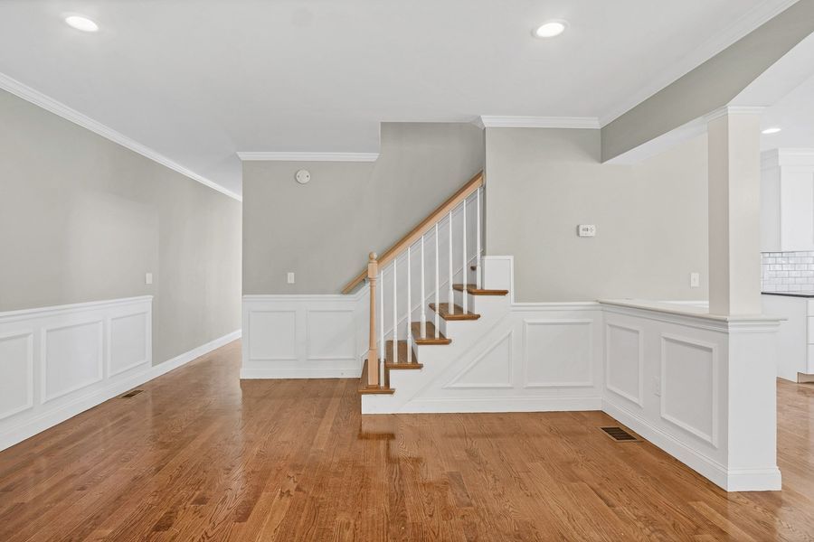 Empty room with wooden floors, staircase, and white wainscoting on gray walls.