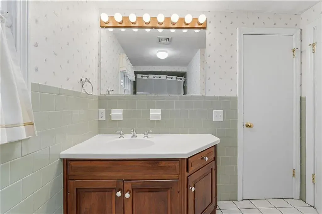 Bathroom with wood vanity, white sink, large mirror, and green tile wainscoting