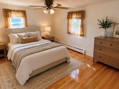 Bright bedroom with a bed, dresser, ceiling fan, and two windows with curtains