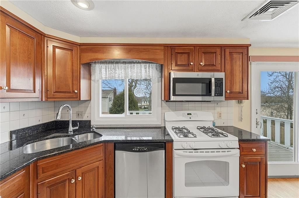 Bright kitchen with wood cabinets, black countertops, white appliances, and a window over the sink