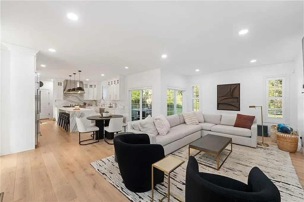 Bright open-concept living room with white sectional, black chairs, rug, and kitchen in the background
