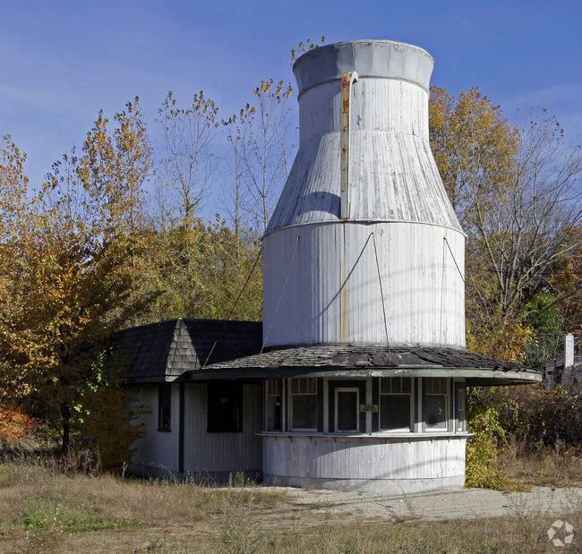 Small abandoned building with a large white cooling-tower structure on top, surrounded by autumn trees.