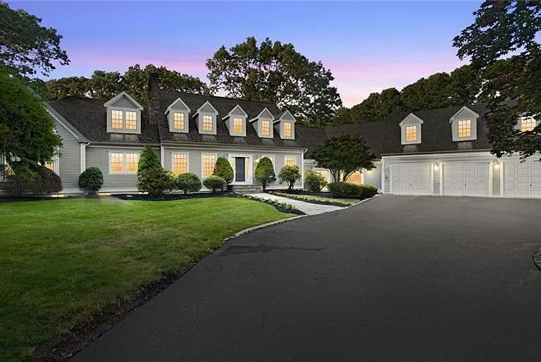 Large gray house with a long driveway and three-car garage, at dusk.