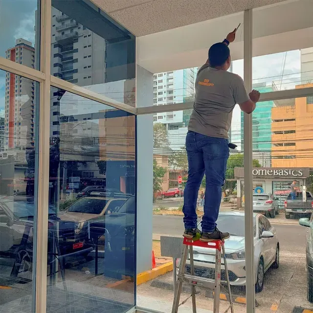 Una persona subida a un taburete pintando el marco de la ventana de una tienda.