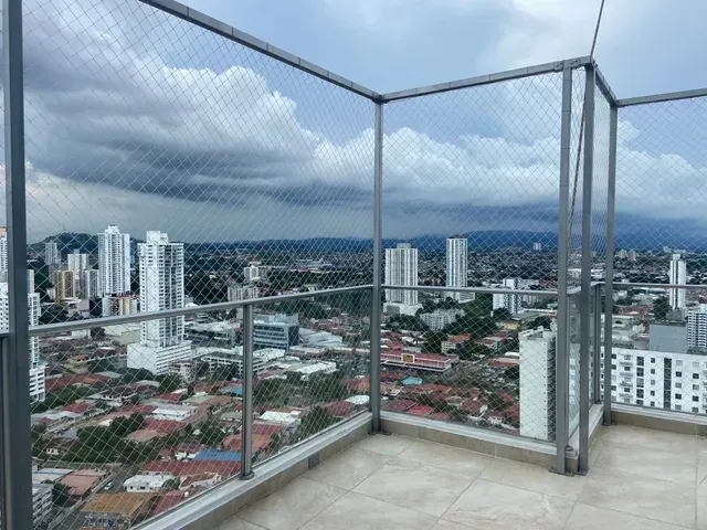 Terraza en la azotea con barandilla de cristal con vistas a un horizonte urbano nublado y a las montañas.