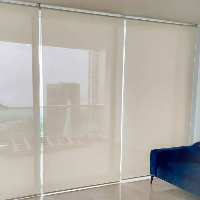 Habitación luminosa con persianas que van desde el suelo hasta el techo y un sofá azul junto a la ventana.
