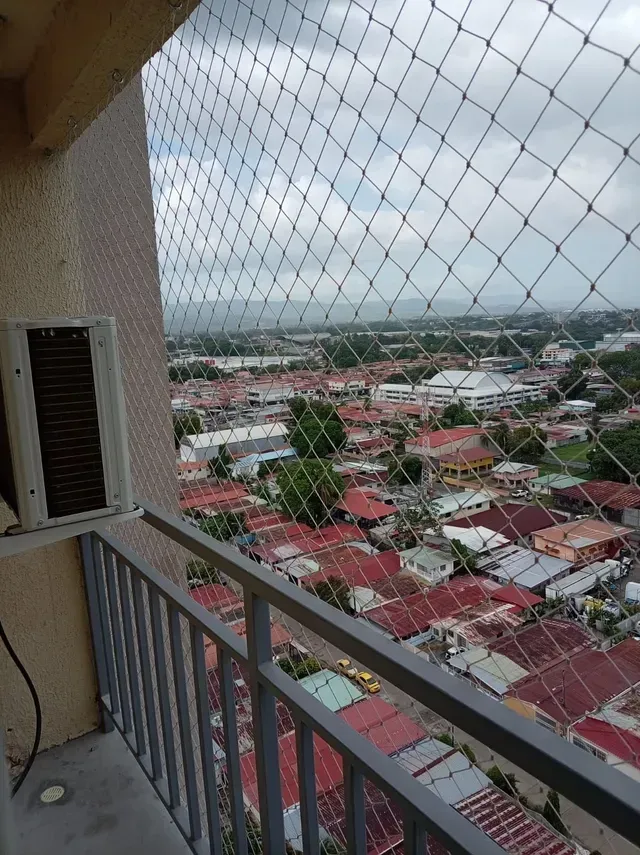 Vista desde un balcón de un pueblo con tejados rojos, redes de malla y cielo nublado.