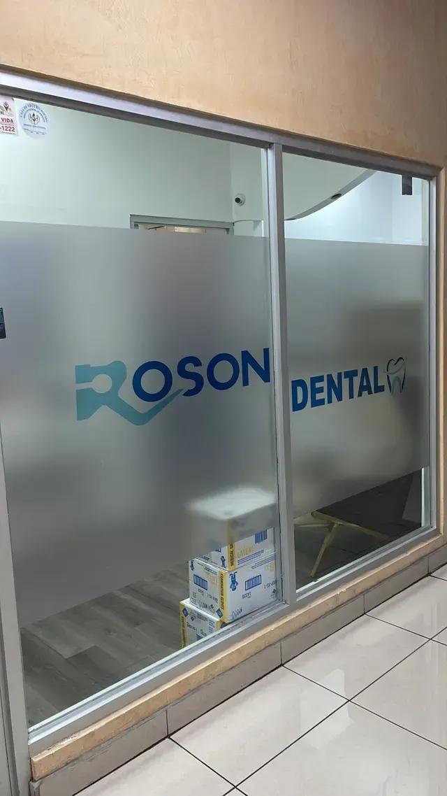 Fachada de cristal esmerilado con la etiqueta “ROSON DENTAL” y una pequeña caja en el suelo.