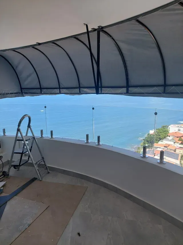Terraza cubierta en la azotea con barandilla de cristal curvada, escalera y vistas al océano a lo lejos.