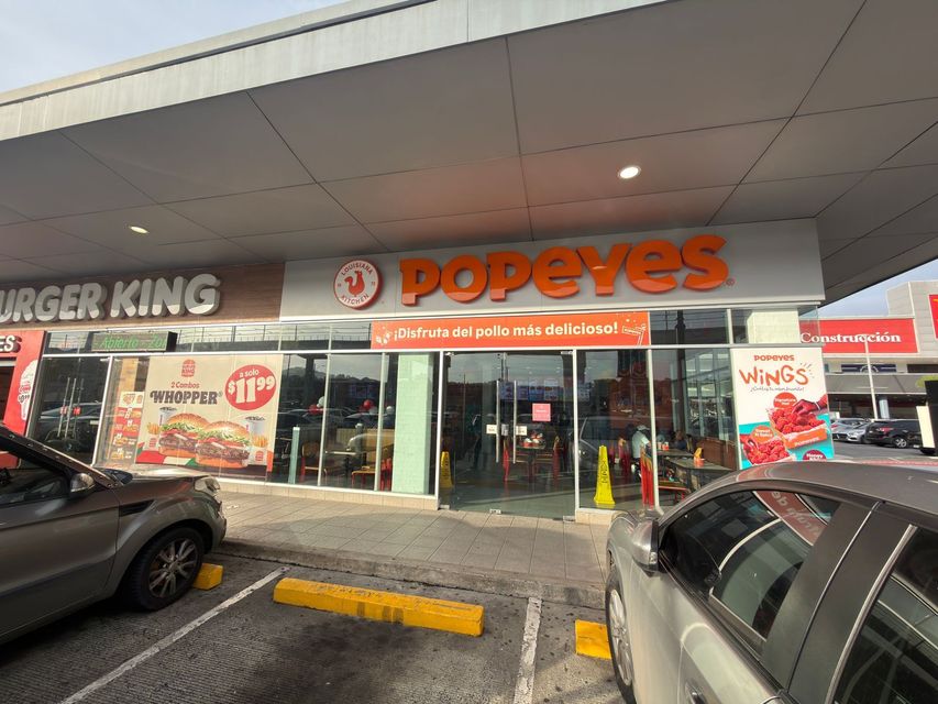 Locales de Burger King y Popeyes en un centro comercial con coches aparcados delante.