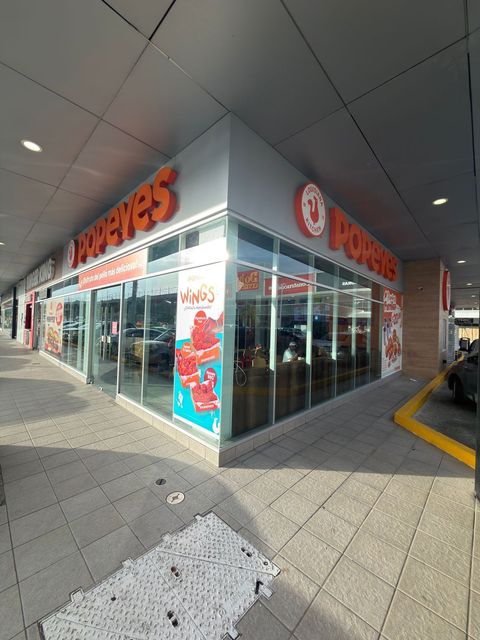 Local comercial de Popeyes en una esquina, con letrero naranja y ventanas de cristal, ubicado en un pasillo cubierto.