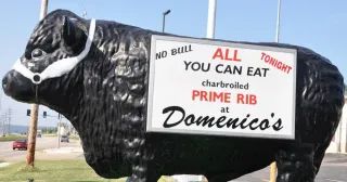 A large, black, statue of a bull wears a white halter and displays a sign advertising prime rib at Domenico’s restaurant.