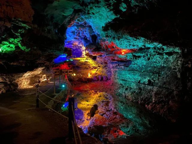A cavern illuminated with vibrant red, green, and blue lights, casting colorful glows on textured rocky surfaces.
