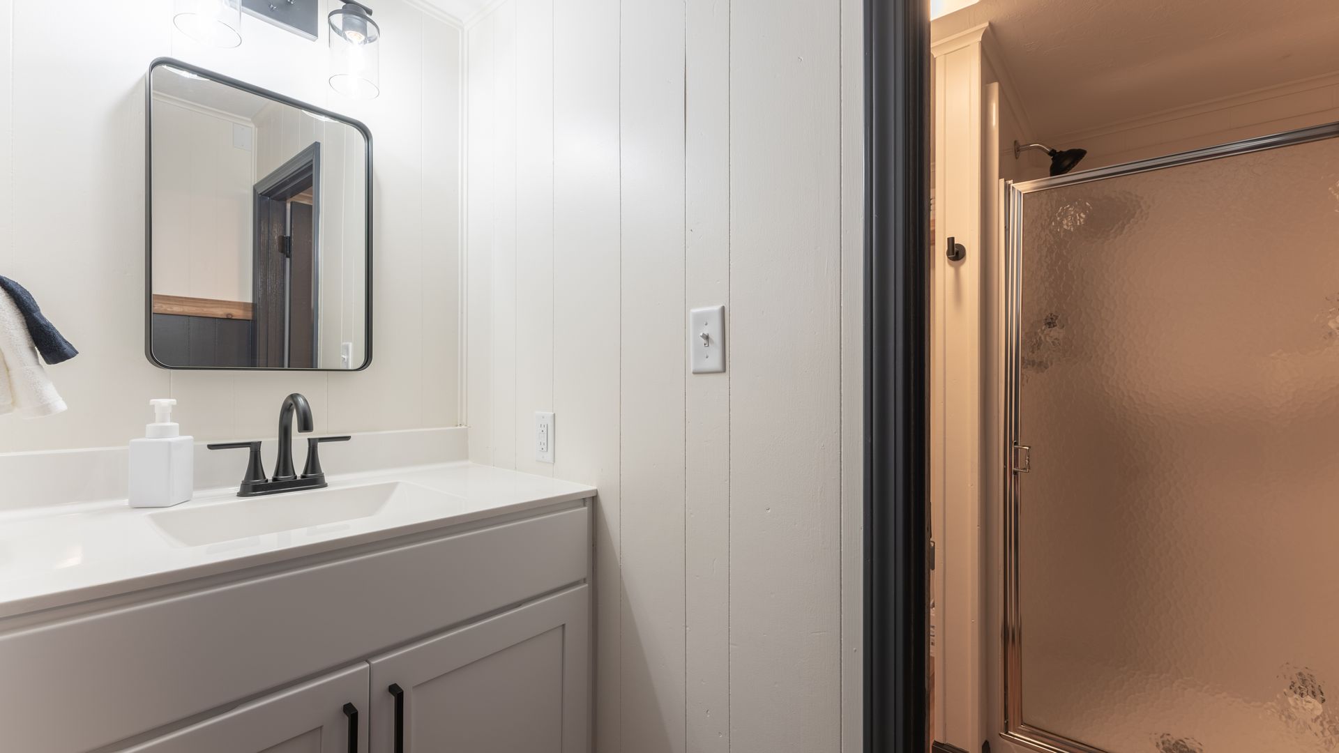 A clean, modern bathroom with a white vanity, a square mirror, and an adjacent tiled shower stall.
