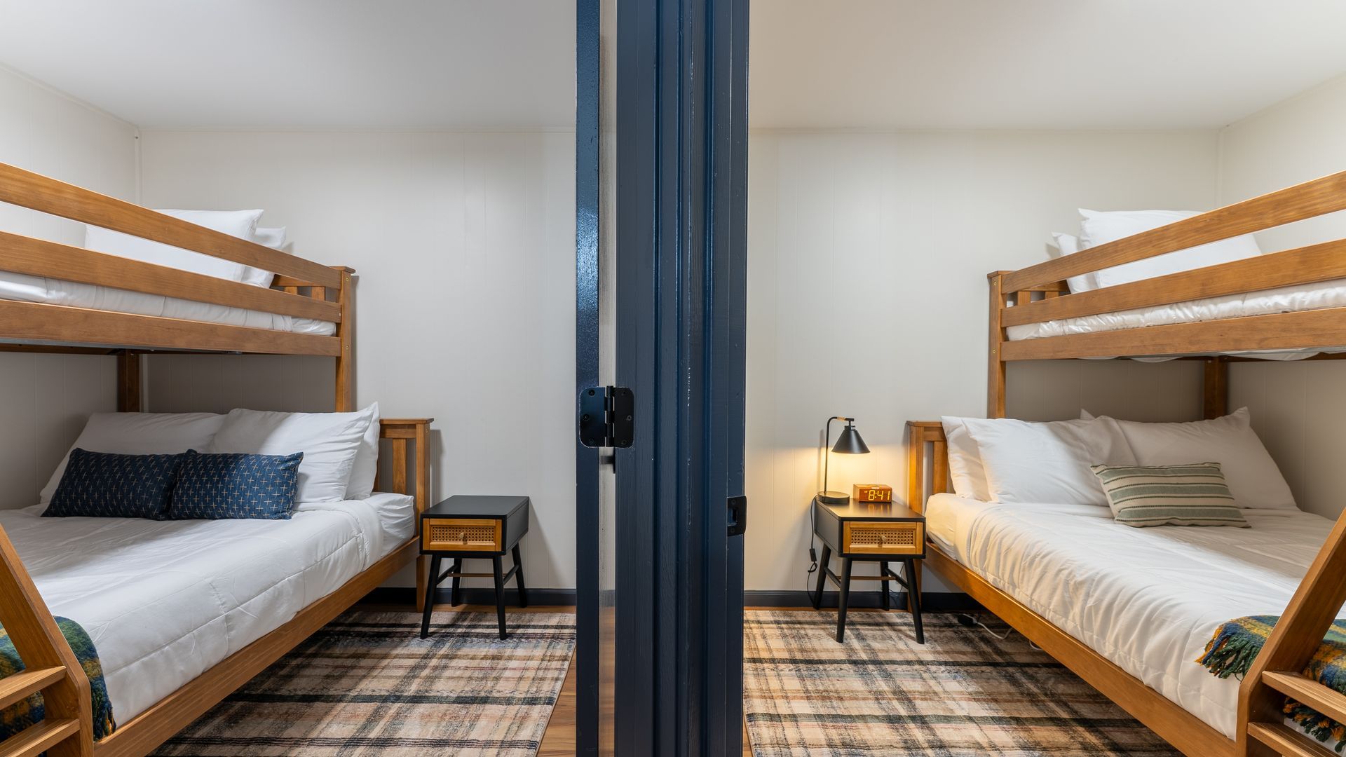 Two wooden bunk bed sets face each other in a room divided by a central pillar, featuring patterned carpet and bedside lamps.