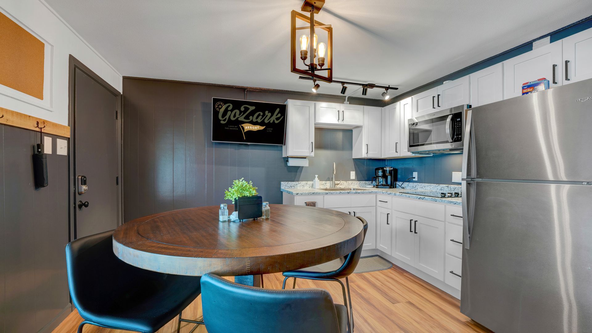 A kitchen and dining area with a round wooden table, two chairs, white cabinets, and stainless steel appliances.
