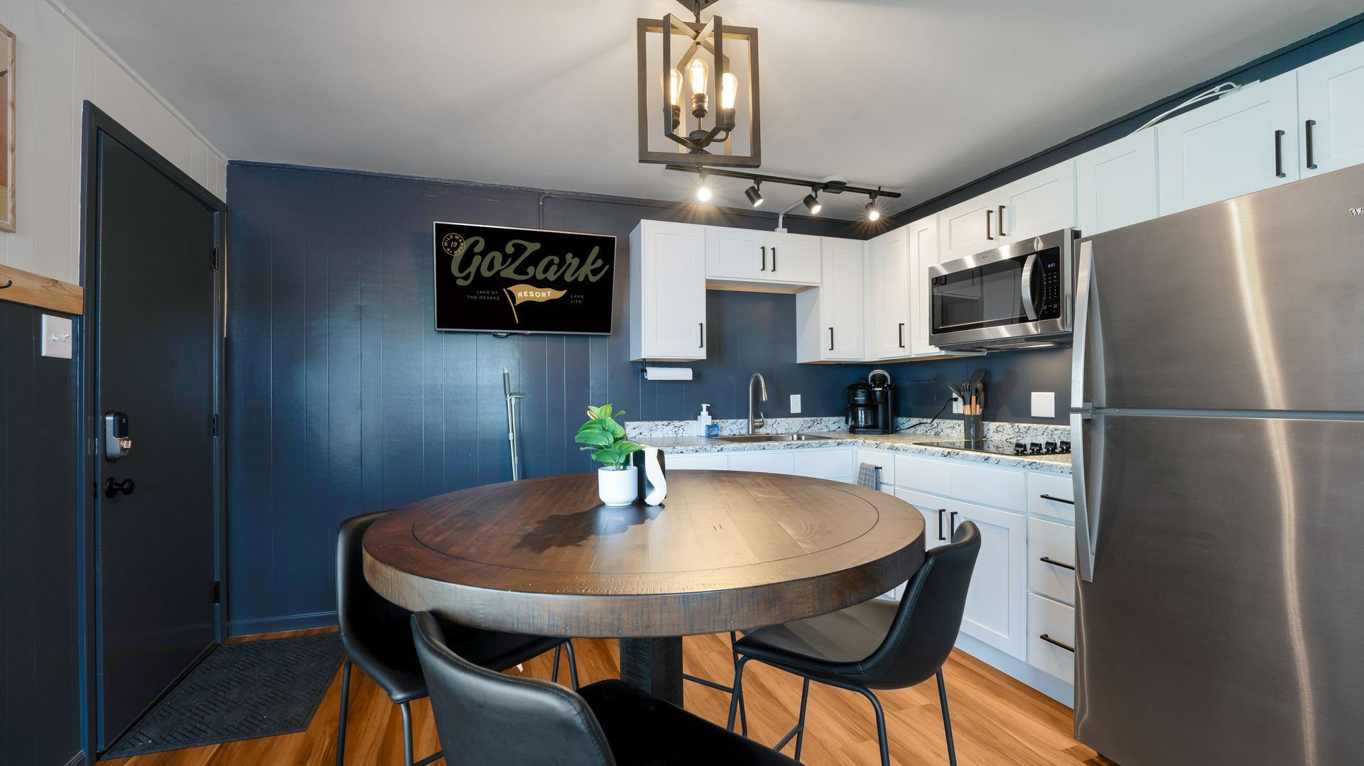 A modern kitchen with white cabinets, stainless appliances, and a round dark wood table in a dark blue room.