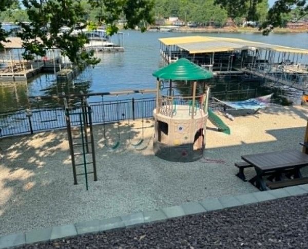 Lakeside playground with a climbing tower, slide, picnic table, and docked boats in the background
