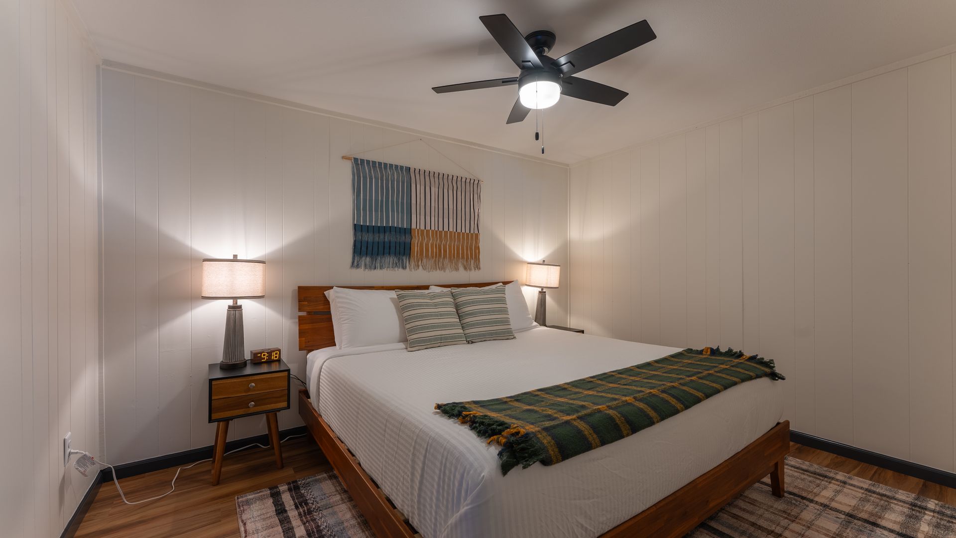 A bedroom with a bed featuring a green plaid blanket, a wooden headboard, two nightstands, and a ceiling fan.
