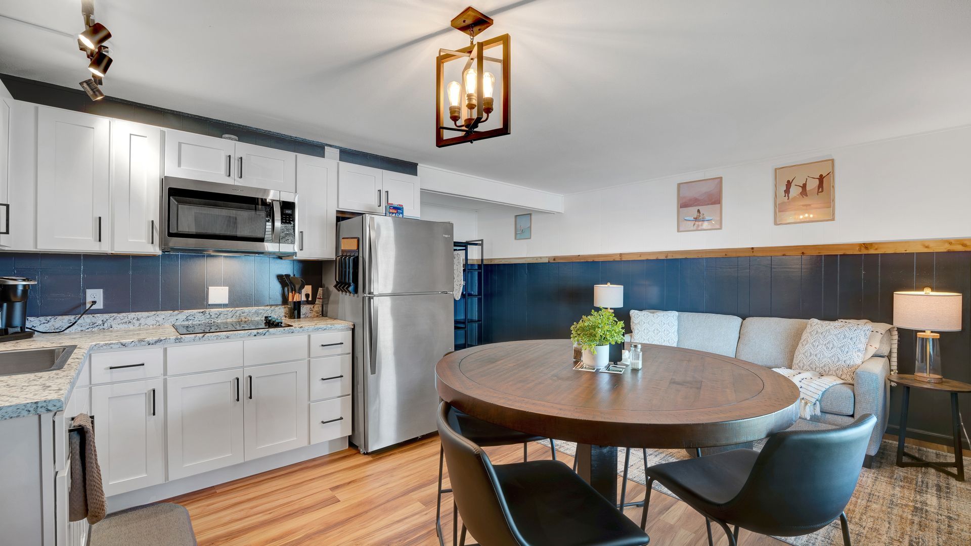 Kitchen and dining area with white cabinets, stainless appliances, round wooden table, and navy blue wall paneling.