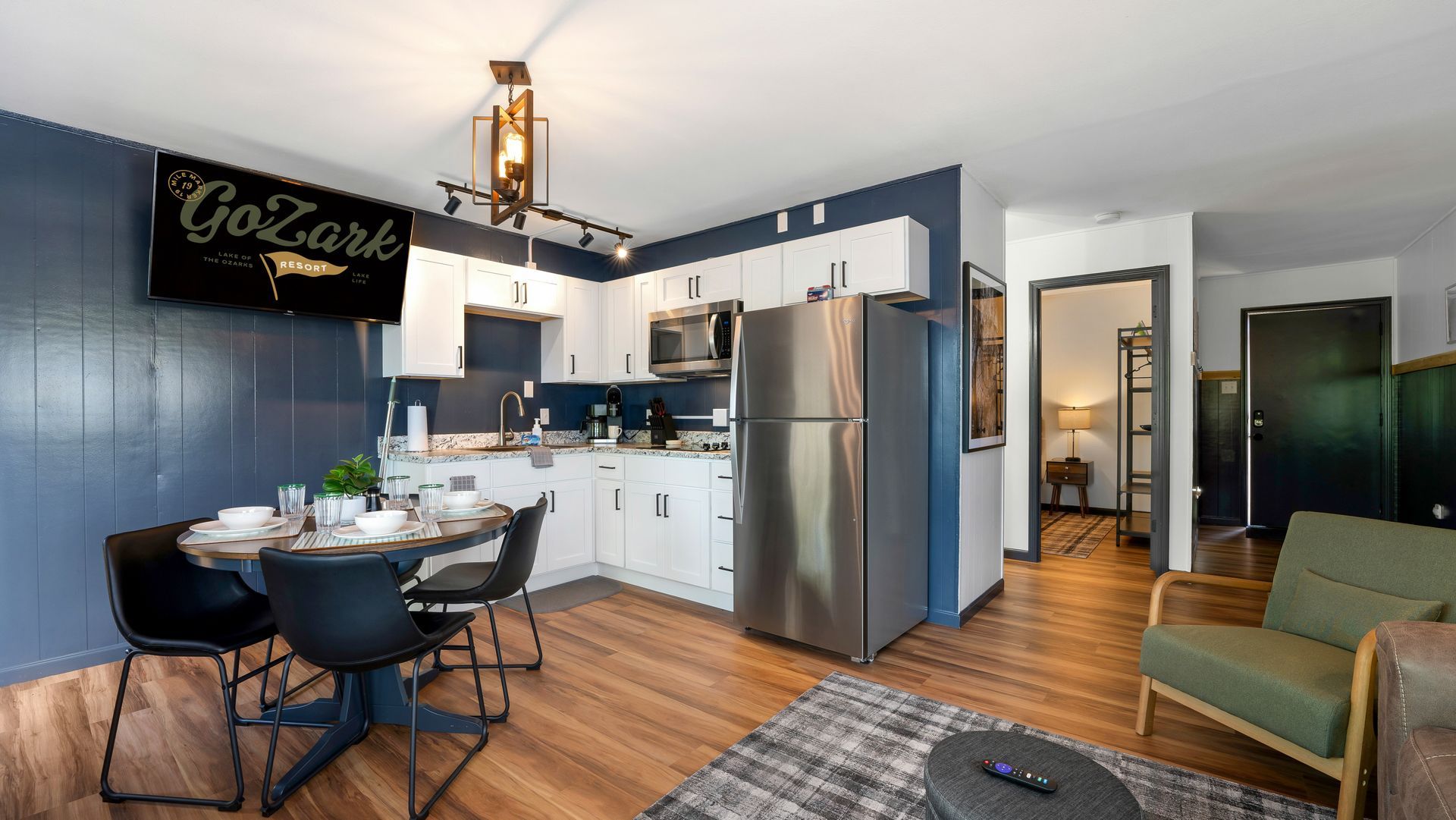 A modern apartment kitchenette with white cabinets, stainless appliances, a dining table, and dark blue accent walls.