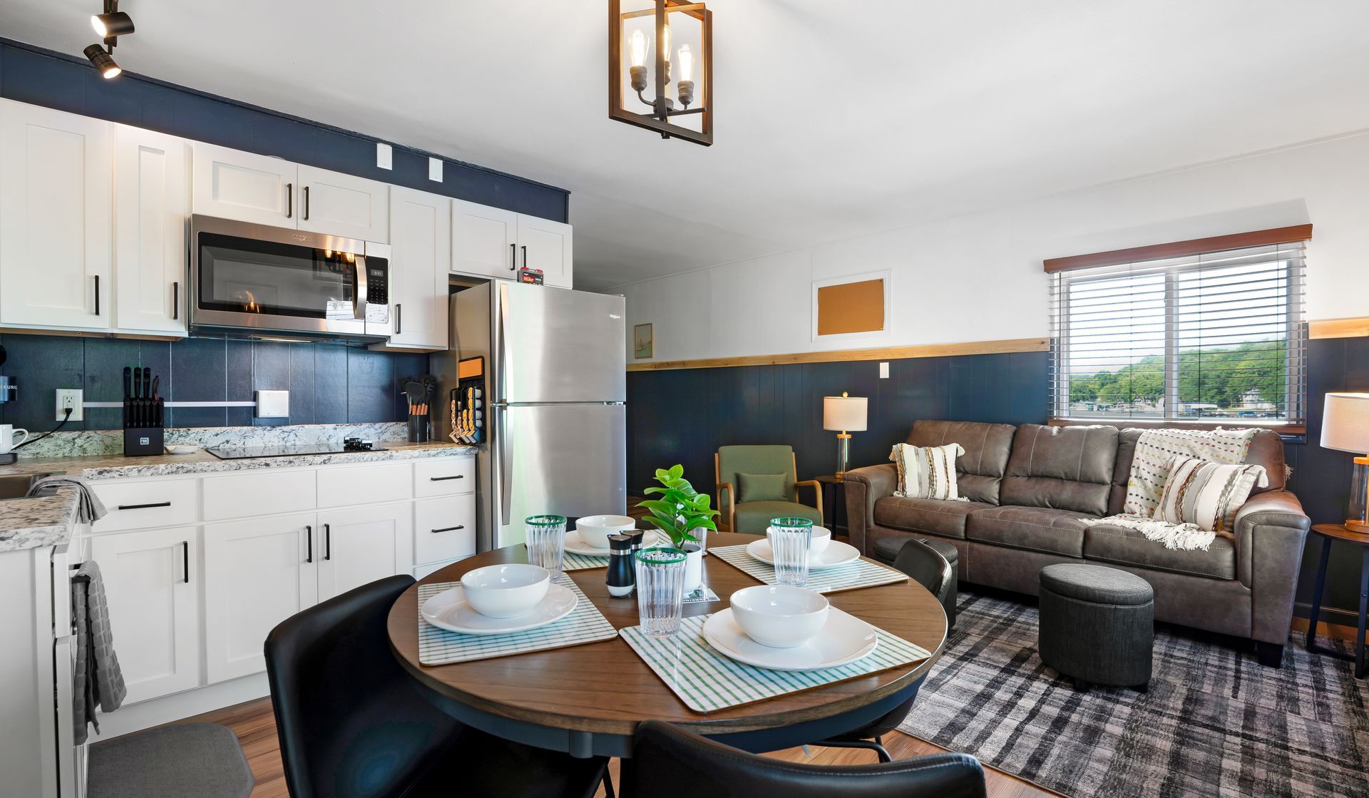 A modern open-plan apartment with white kitchen cabinets, a dining table, and a brown sofa in the living area.
